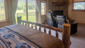 A bedroom with a bed, a stone fireplace, two leather chairs, and large windows with curtains. - 3-bedroom townhome on Golf Course, Perfect Basecamp for Adventure or Relaxing (South Fork)