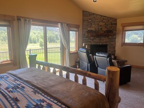 A bedroom with a bed, a stone fireplace, two leather chairs, and large windows with curtains. - 3-bedroom townhome on Golf Course, Perfect Basecamp for Adventure or Relaxing (South Fork)