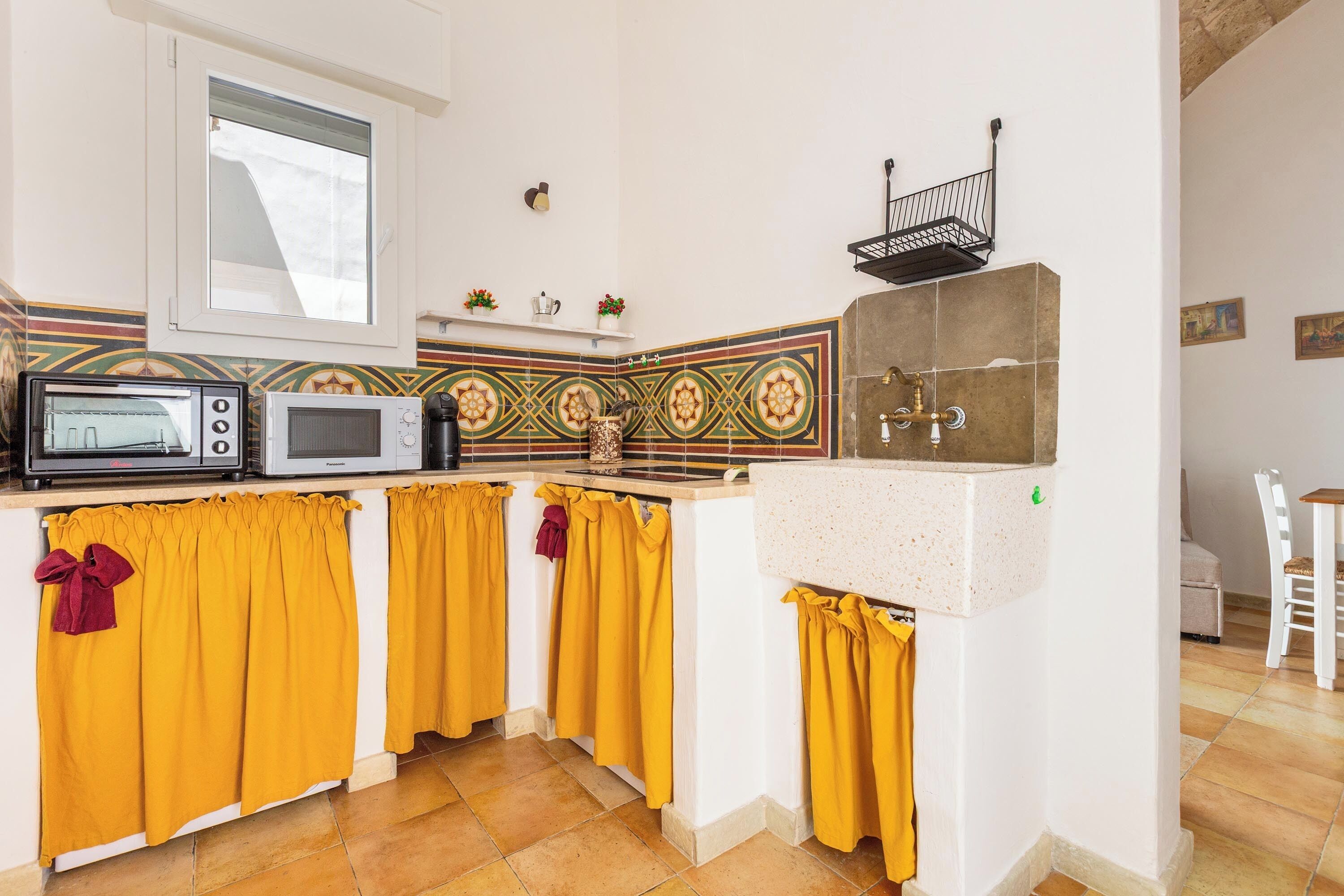 A kitchen with a microwave, stove, and sink. There is a window above the sink and a shelf with decorative items.