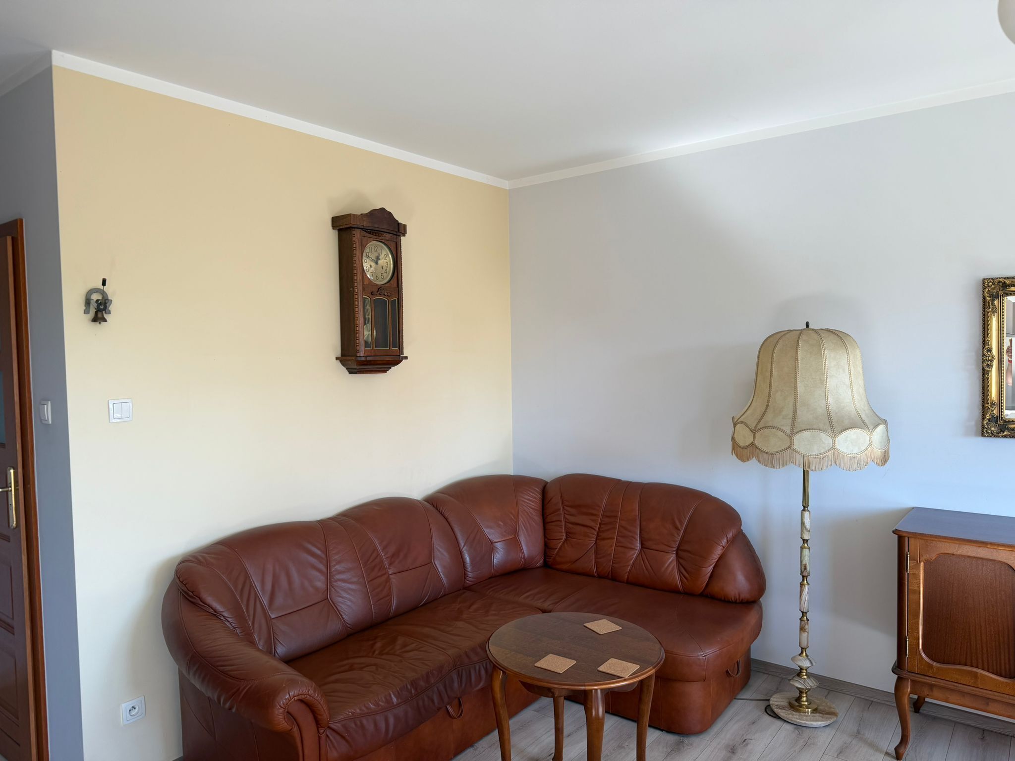 Un canapé en cuir marron, une petite table ronde, un lampadaire, une horloge et un meuble dans une pièce aux murs de couleur beige.
