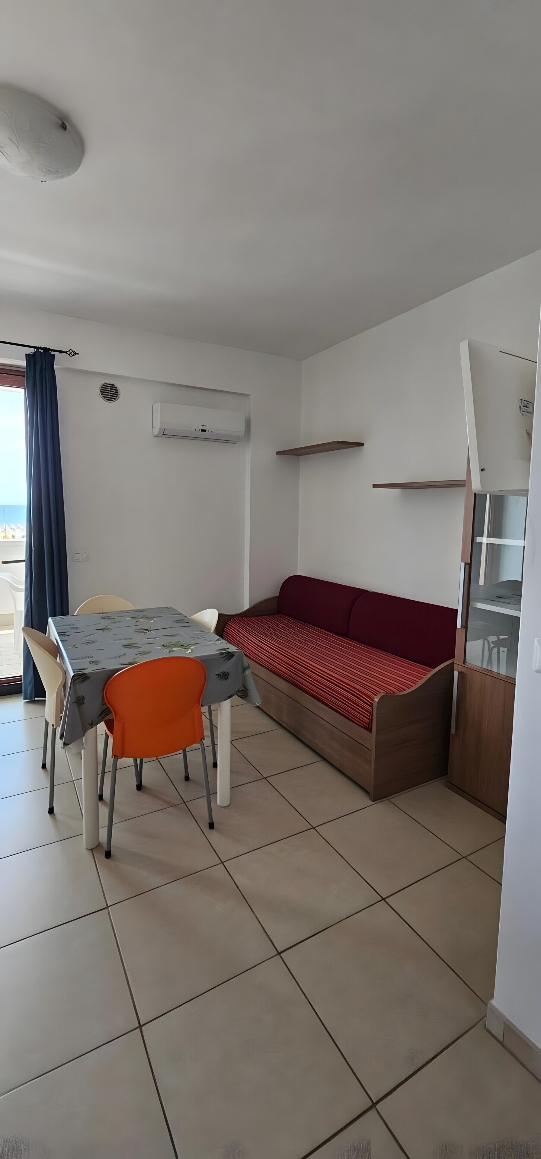 Ein Zimmer mit Esstisch, Stühlen, einer Couch, einer Klimaanlage und einem Fenster mit Vorhängen.