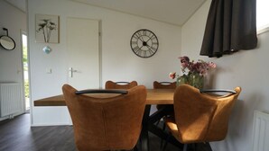 A dining area with a wooden table, four brown chairs, a wall clock, a vase with flowers, and a door. - Holiday Home in Dordrecht With Terrace (Dordrecht)