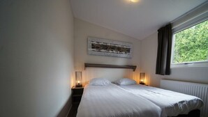 A bedroom with a bed, bedside lamps, a window with curtains, and a wall-mounted artwork. - Holiday Home in Dordrecht With Terrace (Dordrecht)