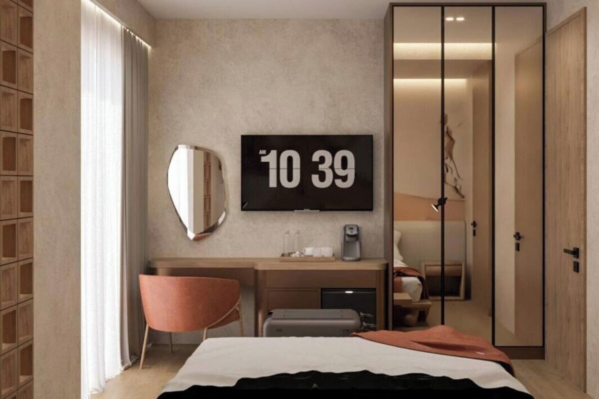 Una habitación de hotel con cama, escritorio, silla, televisor y armario.