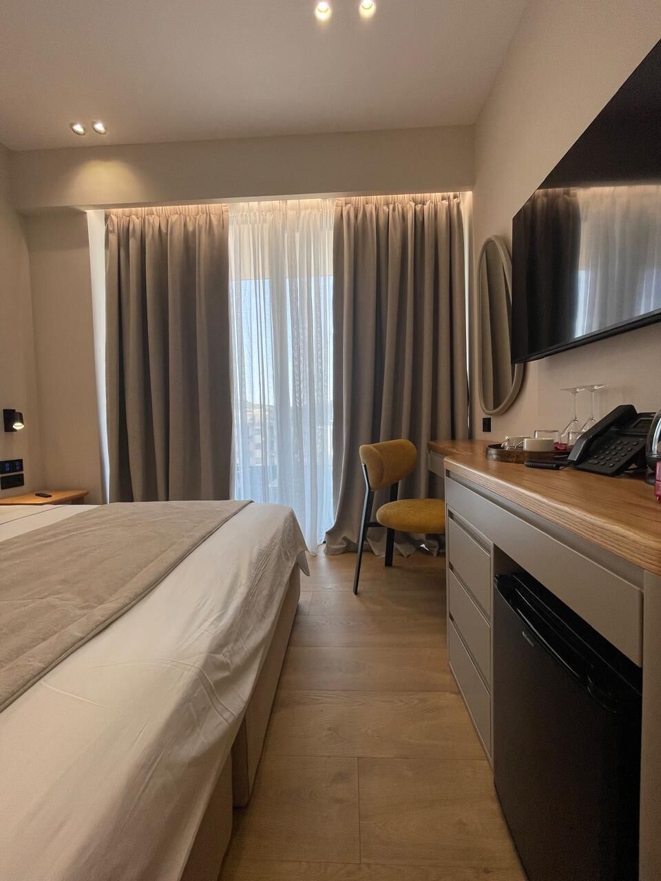 Habitación de hotel con cama, escritorio con teléfono, silla, televisor y ventana con cortinas.