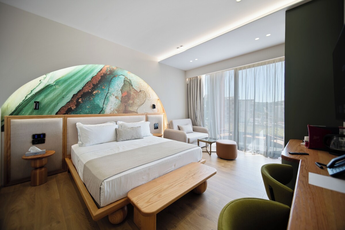 A modern hotel room with a large bed, a seating area, and a view of the city.