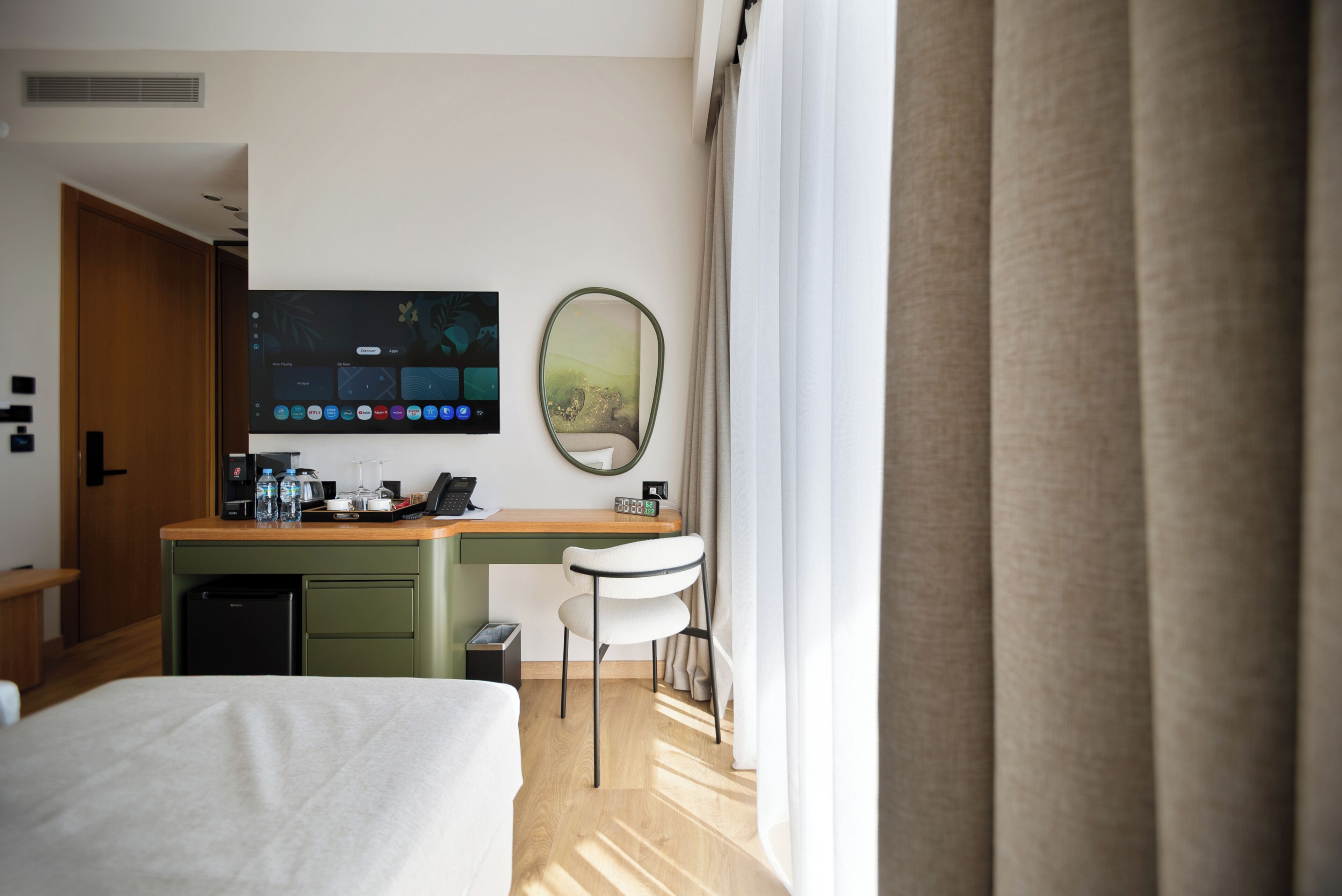 Une chambre d’hôtel avec un lit, un bureau doté d’un écran d’ordinateur, une chaise et une fenêtre avec des rideaux.