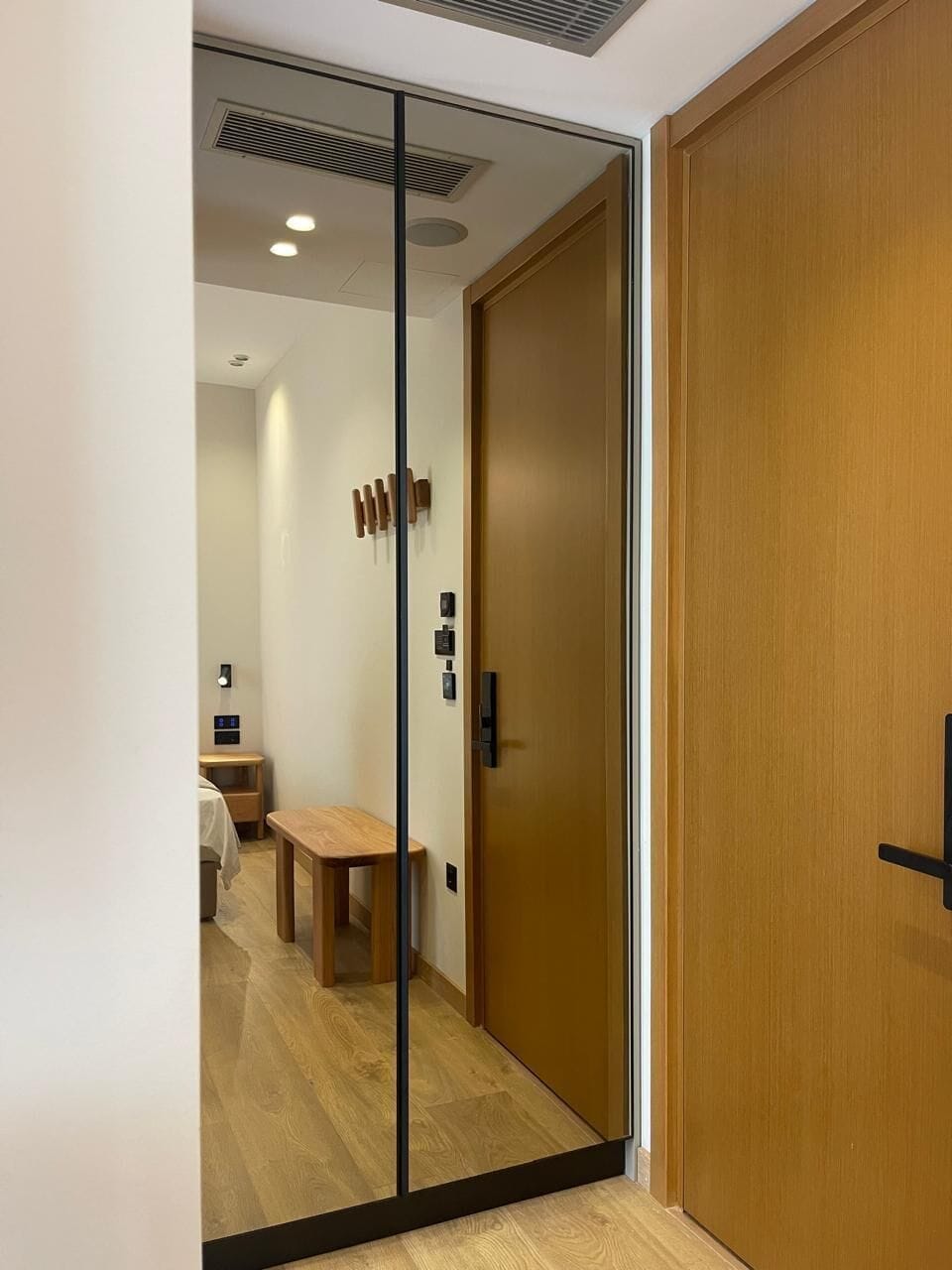Un interno moderno con una porta scorrevole in vetro che dà su un ambiente con pavimento in legno, una panca e un tavolino.