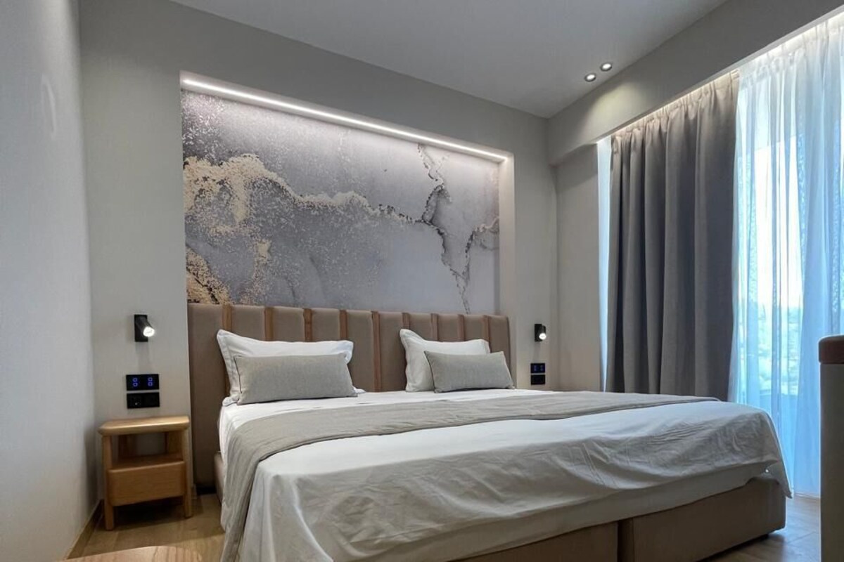 A modern bedroom with a large bed, a nightstand, a wall-mounted light, and a window with curtains.