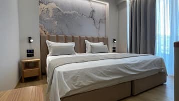 A modern bedroom with a large bed, a nightstand, a wall-mounted light, and a window with curtains.