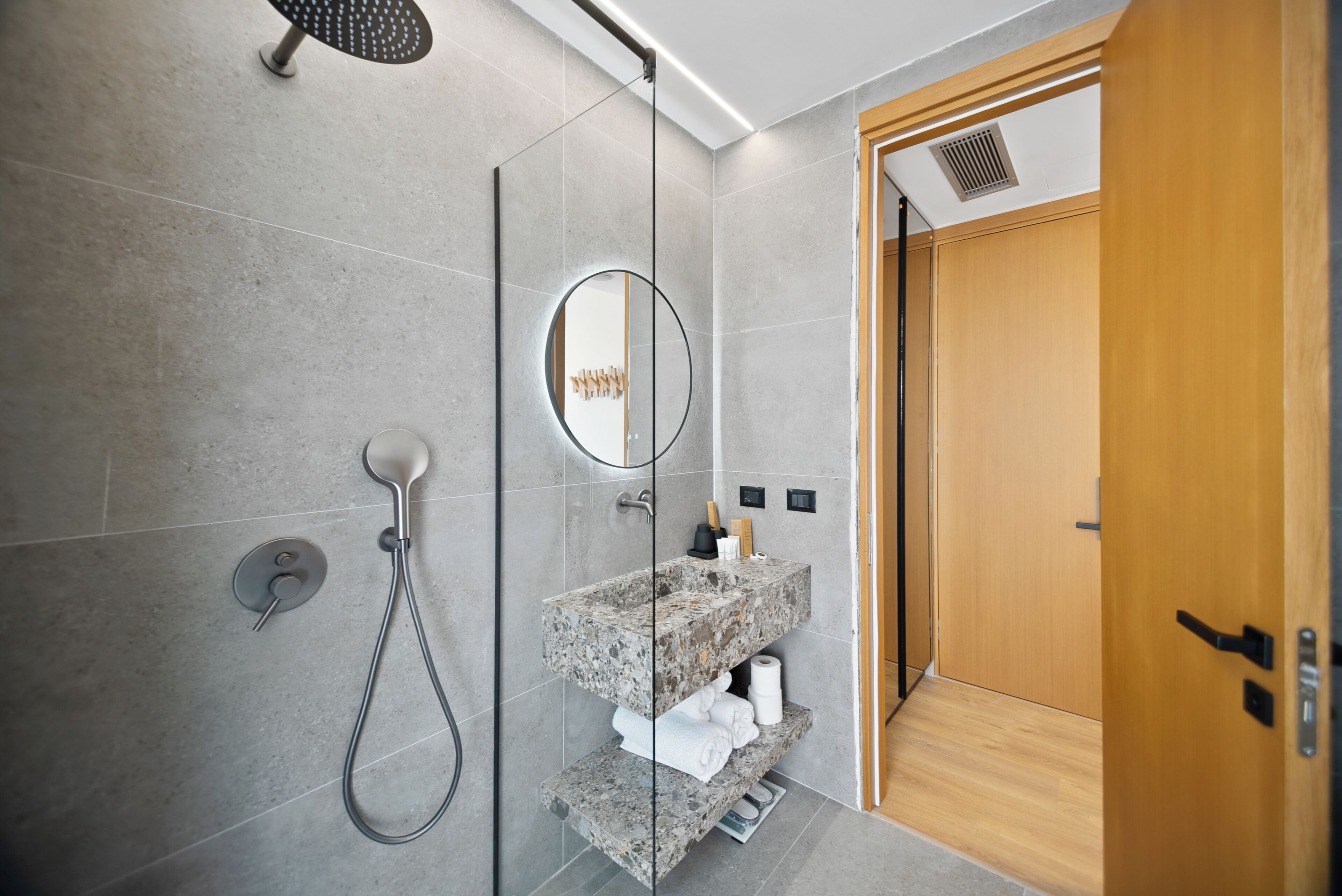 Un baño moderno con ducha envuelta en vidrio, encimera de granito y puerta de madera.
