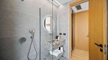 Un baño moderno con ducha envuelta en vidrio, encimera de granito y puerta de madera.