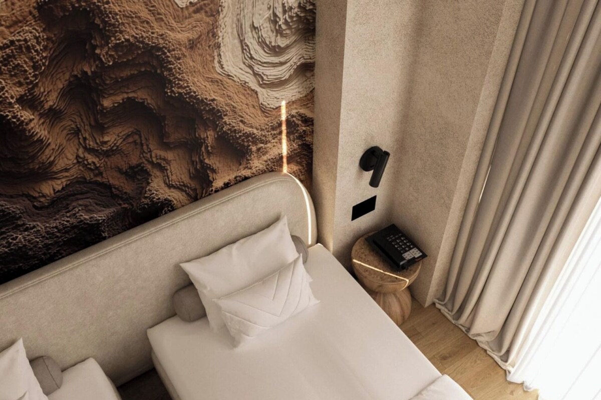 Una habitación de hotel con una cama, una mesita de noche con un control remoto y una pared con textura.
