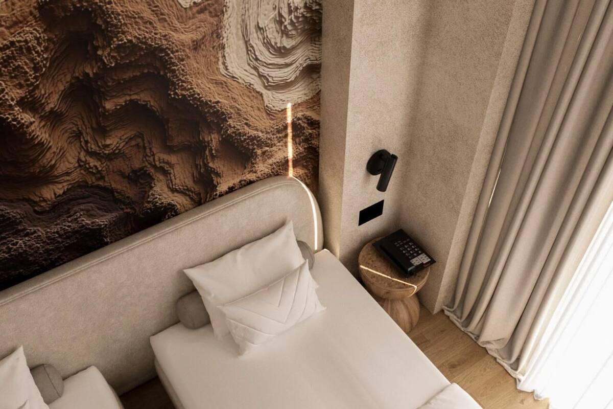 Habitación de hotel con cama, almohadas, mesita de noche con teléfono y pared con textura.