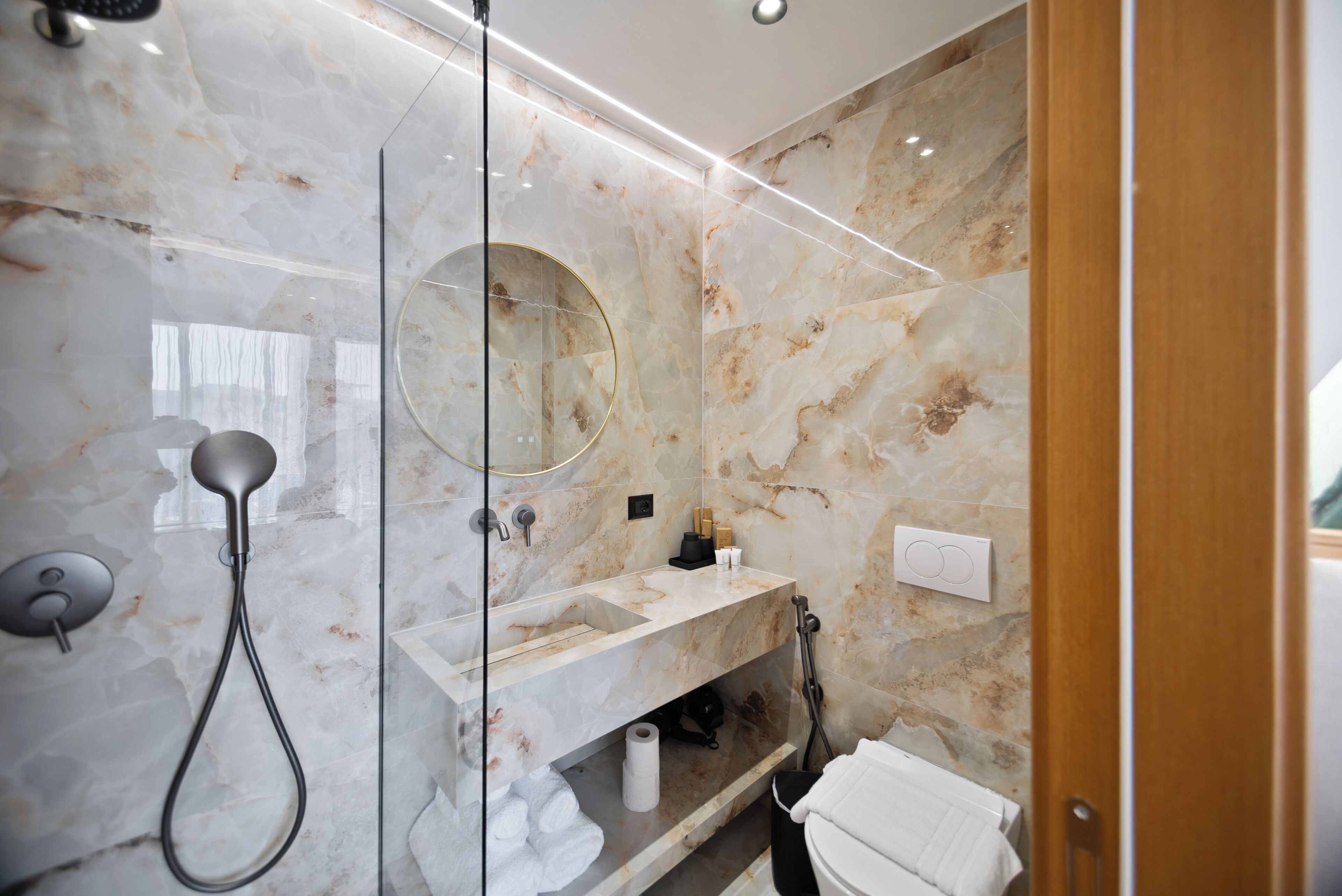 Un baño moderno con ducha envuelta en vidrio, tocador de mármol e inodoro integrado.