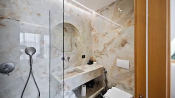 Un baño moderno con ducha envuelta en vidrio, tocador de mármol e inodoro integrado.