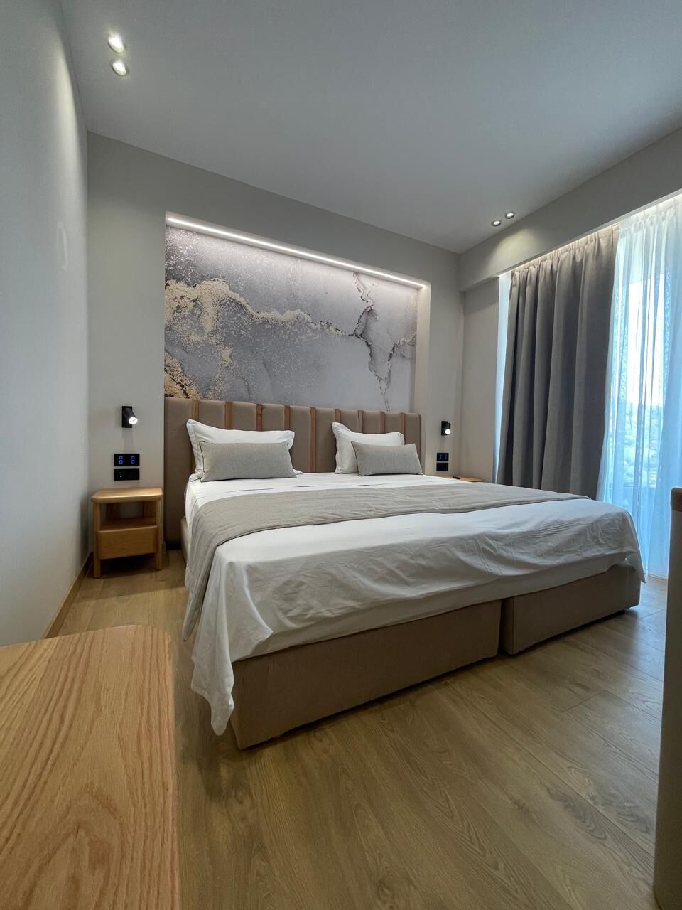 Une chambre moderne avec un grand lit, un plancher en bois, un mur en marbre et une fenêtre avec des rideaux.