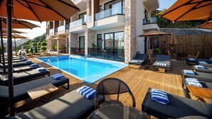 Zona de piscina con tumbonas y sombrillas, una piscina azul cristalina y un edificio moderno con balcones.