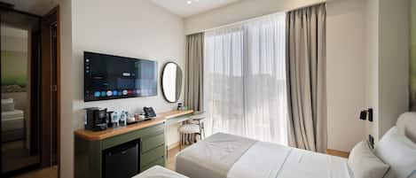 Ein Hotelzimmer mit einem Bett, einem Schreibtisch mit Kaffeemaschine, einem Fernseher und einem Fenster mit Vorhängen.