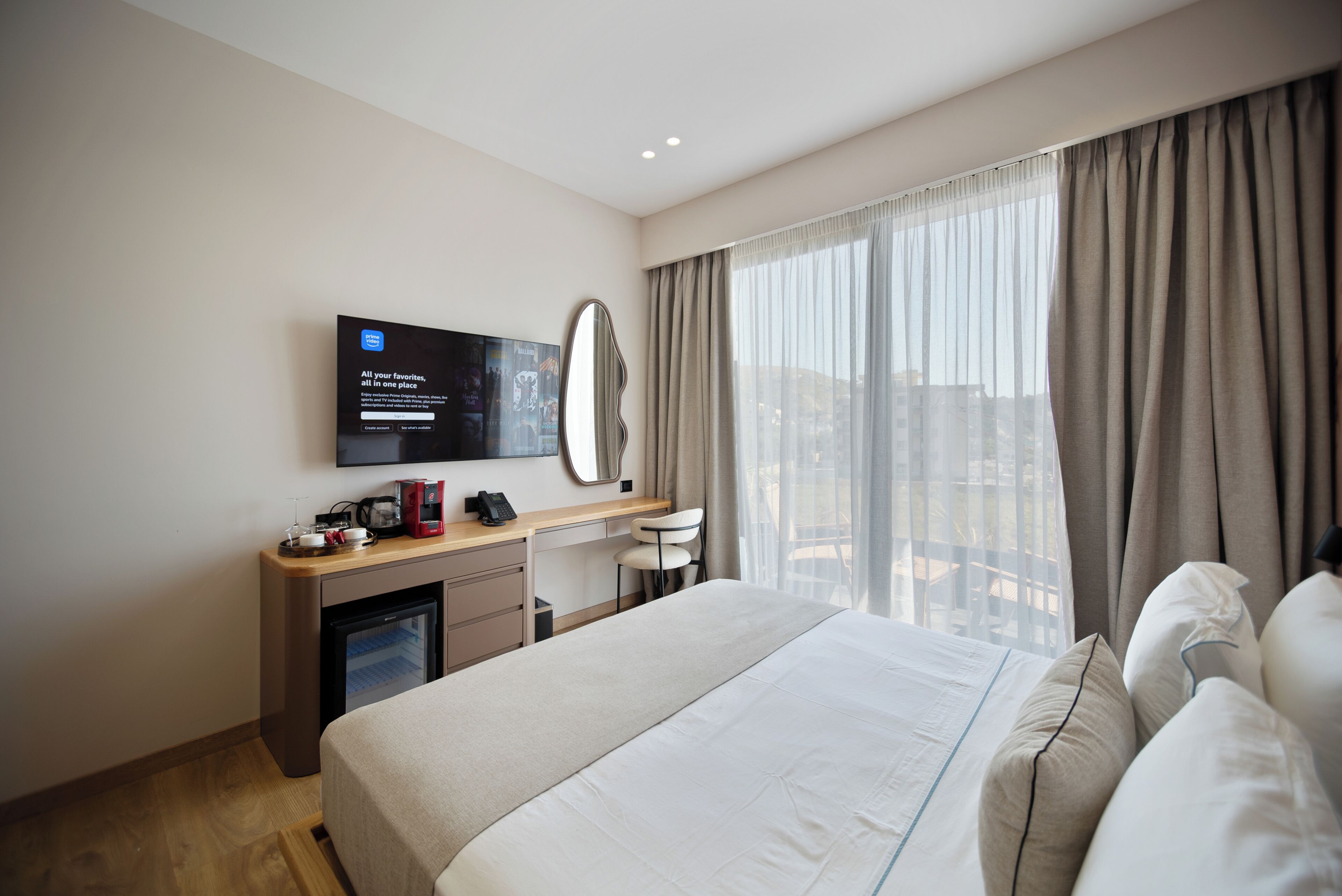 Una habitación de hotel con una cama, un escritorio con computadora, un televisor y un ventanal con cortinas.