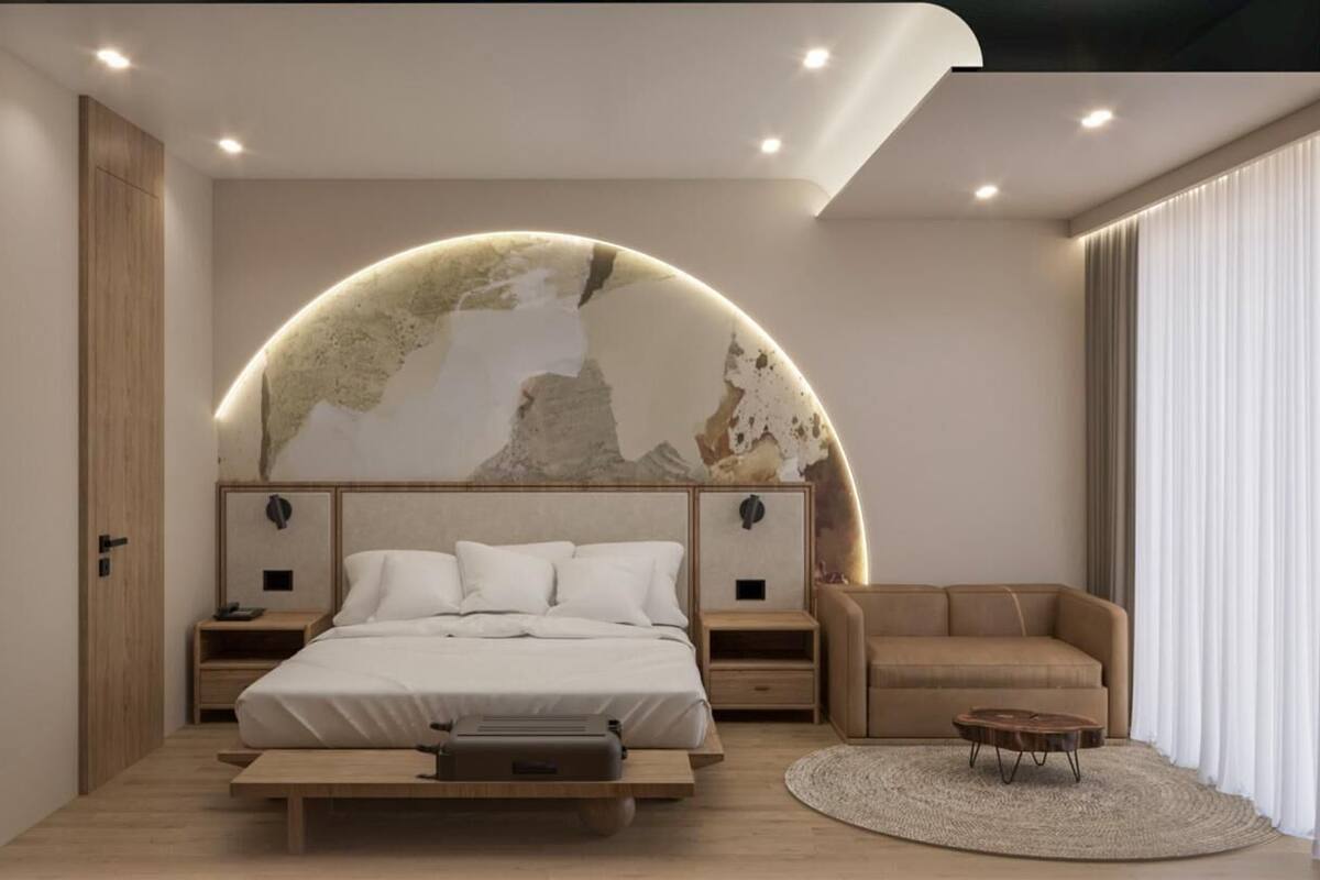 Un dormitorio moderno con un elemento decorativo de pared curva, una cama, una mesita de noche, un sofá y una mesa de centro redonda.
