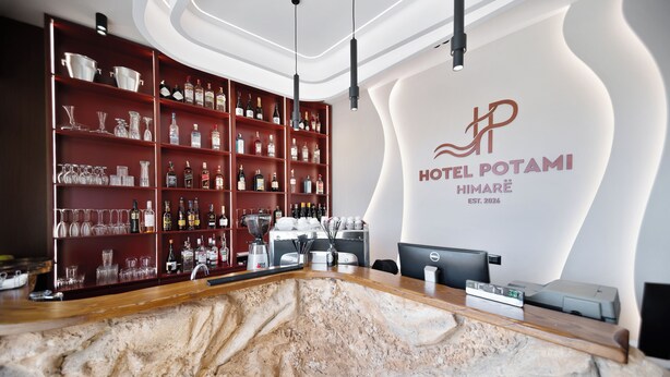 Zona de recepción de un hotel con mostrador de mármol, estantes con botellas de licores y un logotipo moderno en la pared.