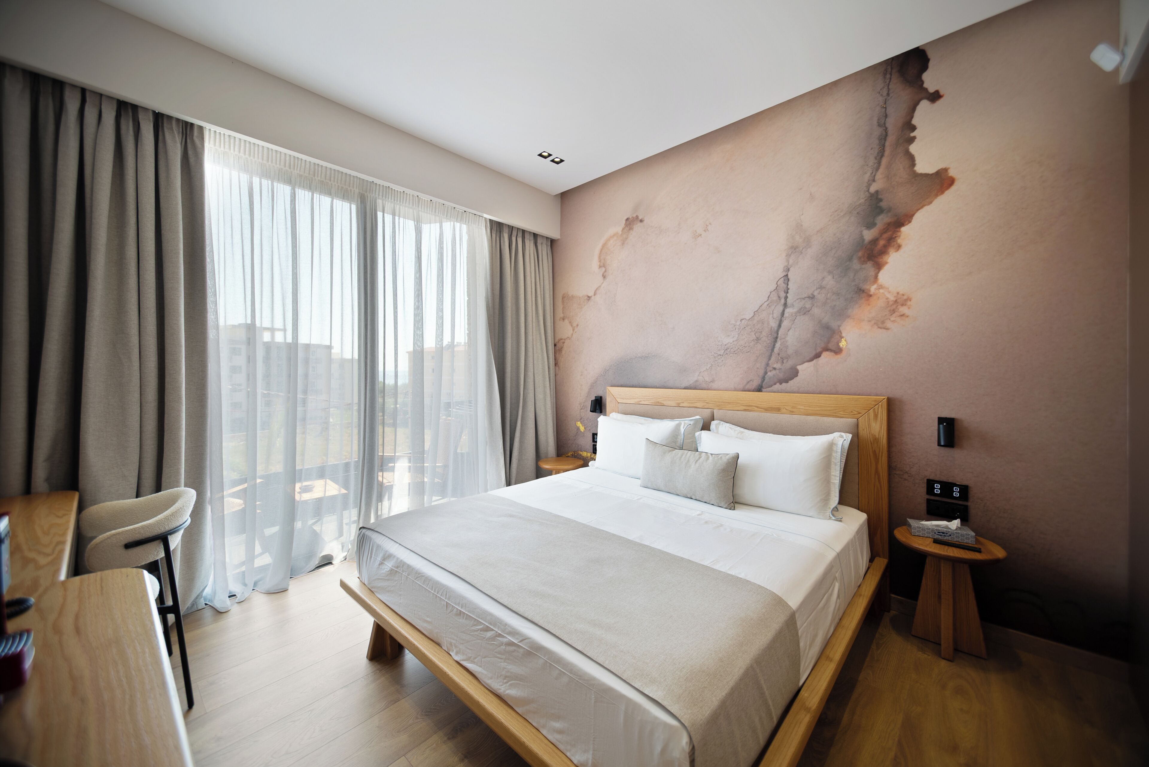 Habitación de hotel con una cama grande, un escritorio y una silla. Se ve el exterior a través de la ventana.