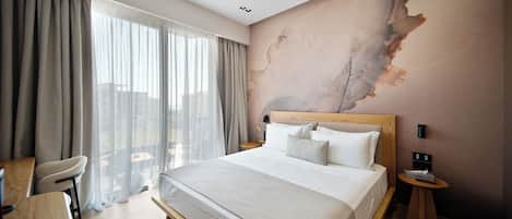 Habitación de hotel con una cama grande, un escritorio y una silla. Se ve el exterior a través de la ventana.