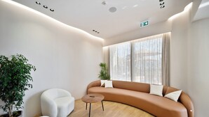 Un interior moderno con un sofá curvo, dos sillones blancos, una pequeña mesa de madera y un gran ventanal con cortinas translúcidas.