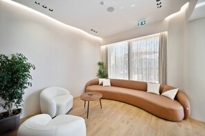 A modern interior with a curved sofa, two white armchairs, a small wooden table, and a large window with sheer curtains.