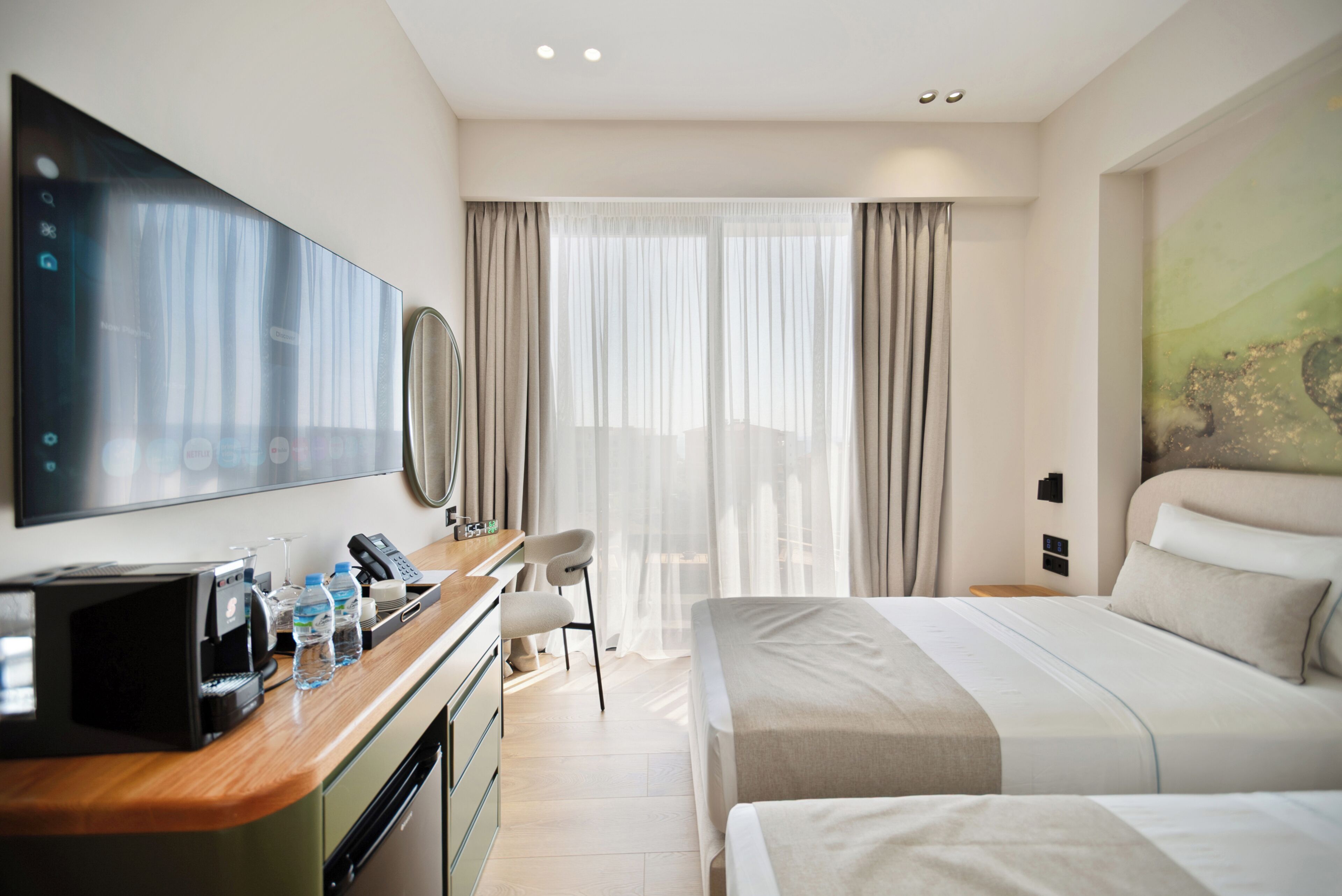 Una habitación de hotel con una cama, un escritorio con teléfono, televisión y ventana con cortinas.