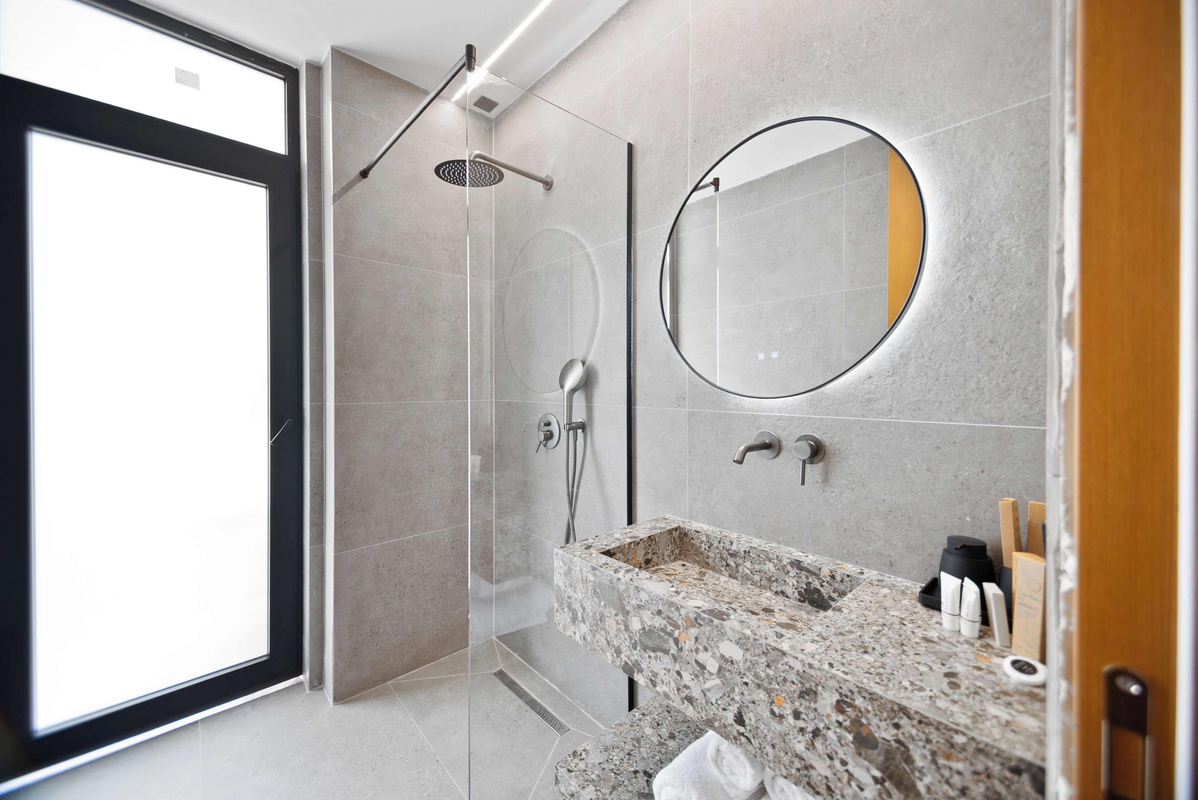 A modern bathroom with a shower, a sink with a granite countertop, and a large mirror.
