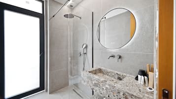 A modern bathroom with a shower, a sink with a granite countertop, and a large mirror.