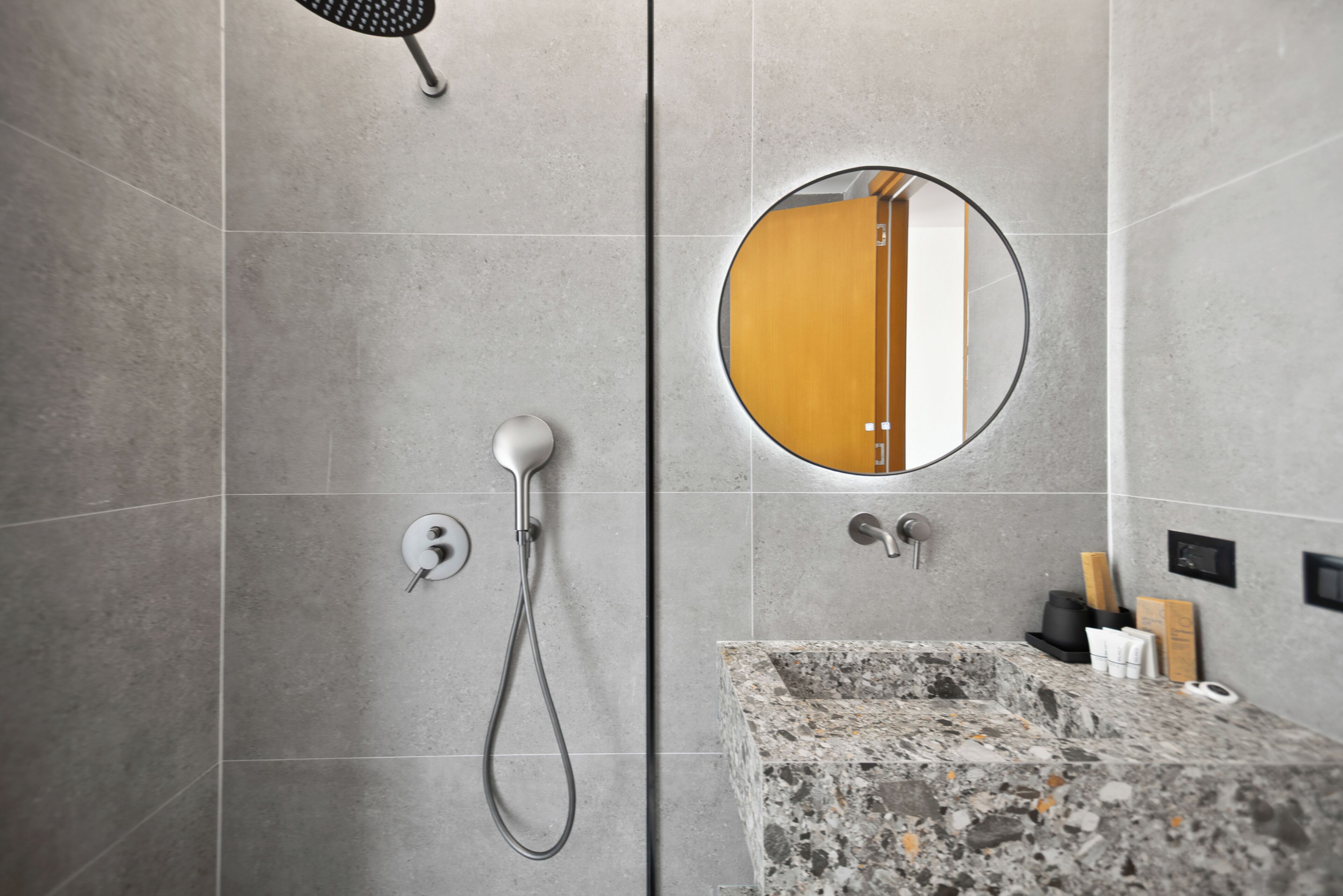 A modern bathroom with a shower, a round mirror, and a granite countertop.