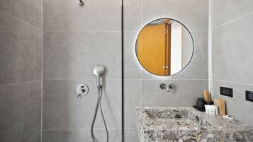 A modern bathroom with a shower, a round mirror, and a granite countertop.