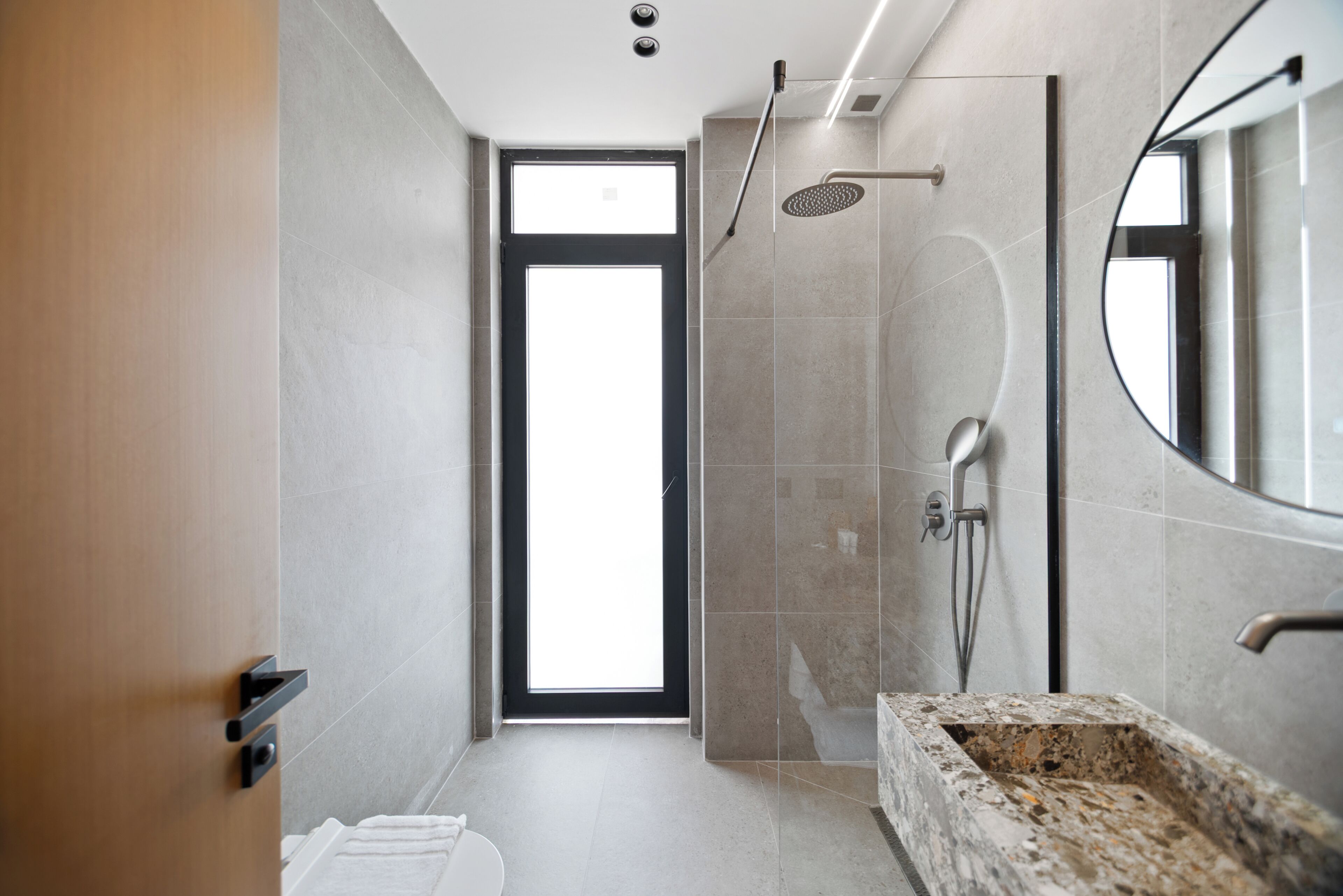 A modern bathroom with a shower, a sink with a marble countertop, and a large mirror.