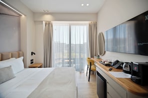 A hotel room with a bed, a desk with a telephone, a television, and a view of the city through large windows.
