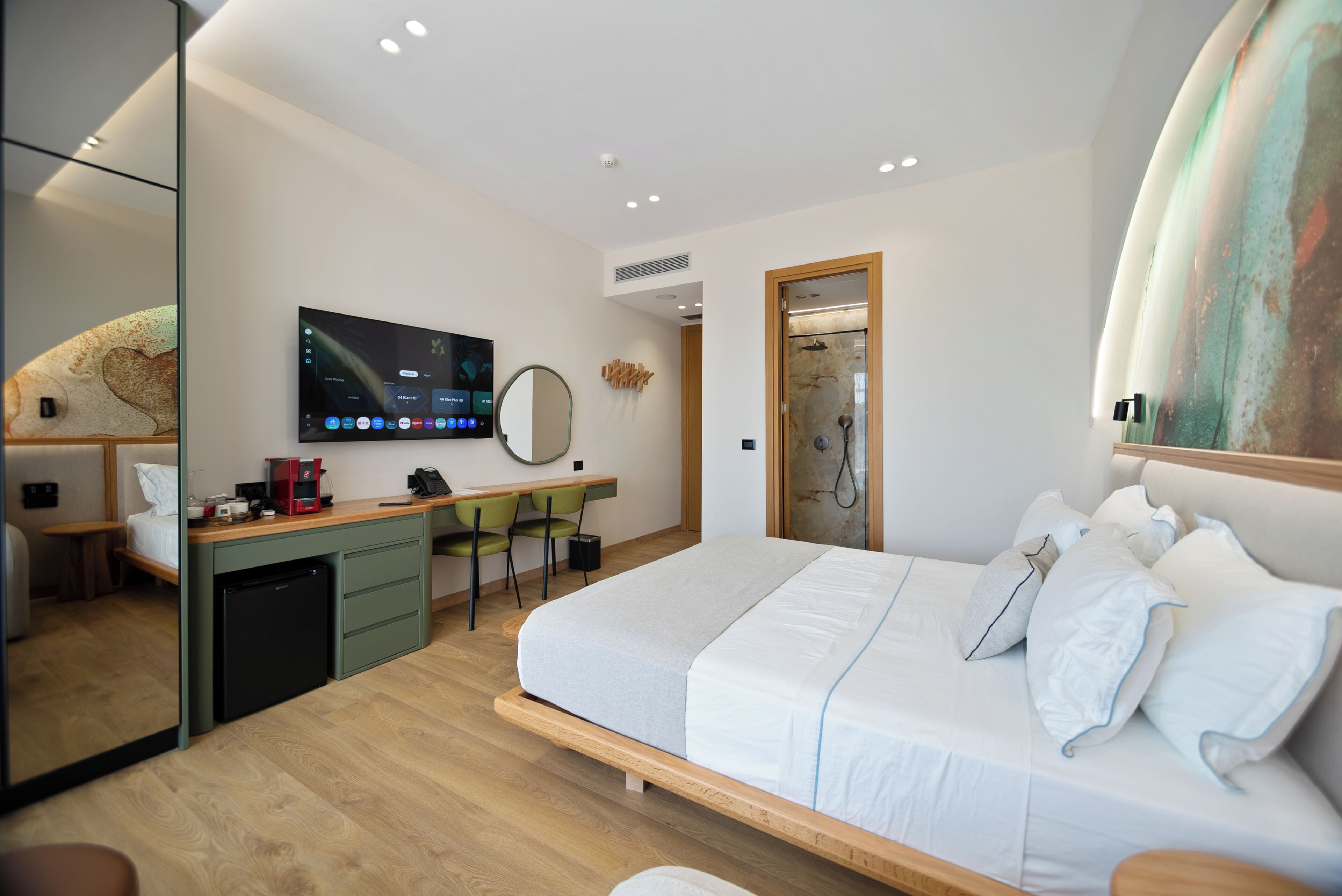 A modern hotel room with a bed, desk, chair, and a television mounted on the wall.
