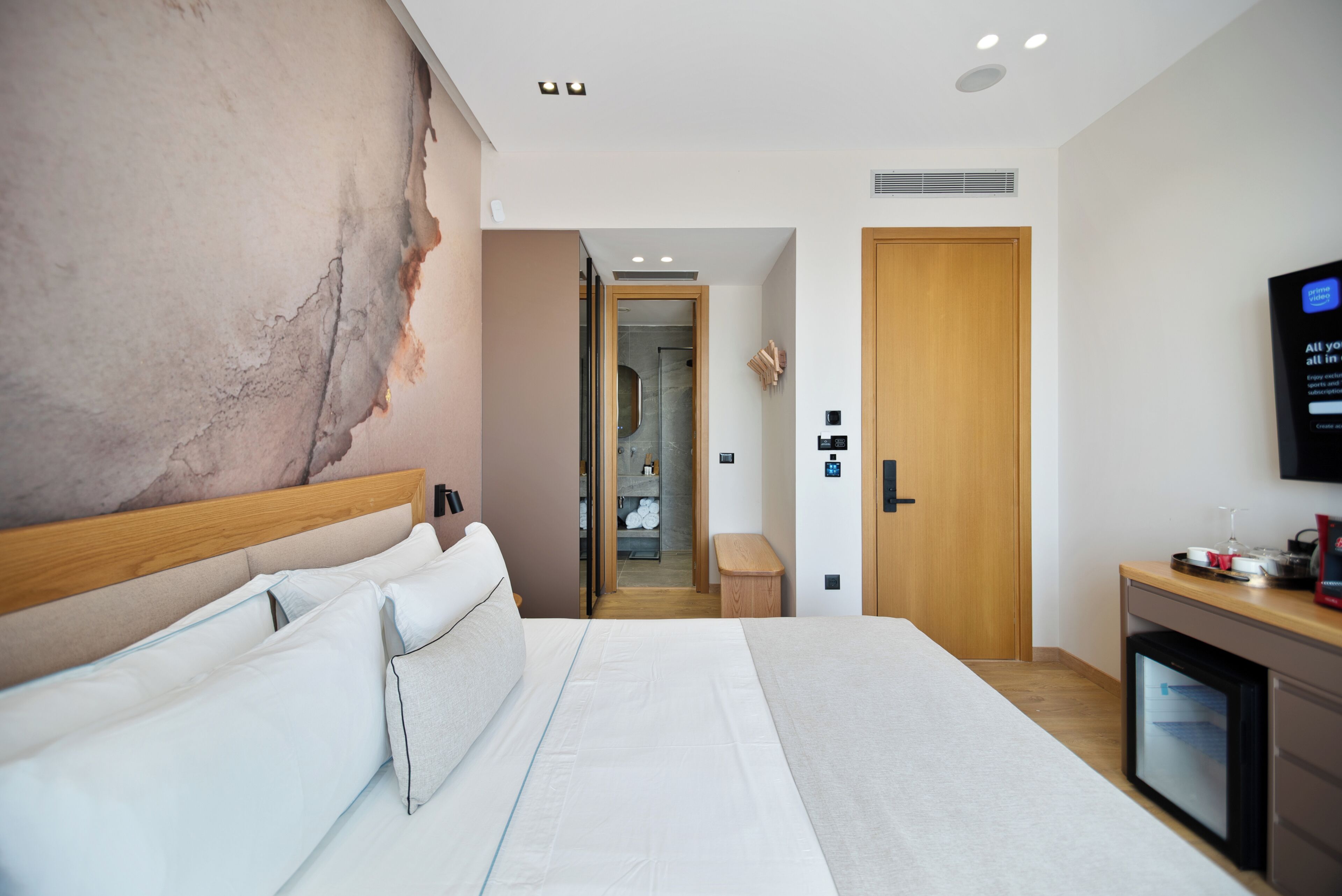 Une chambre d’hôtel moderne avec un grand lit, une tête de lit en bois, une télévision et un minibar.