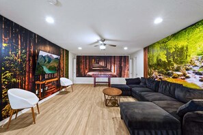 Ein modernes Wohnzimmer mit großem Flachbildfernseher, einer Couch, einem Couchtisch und einem Deckenventilator.