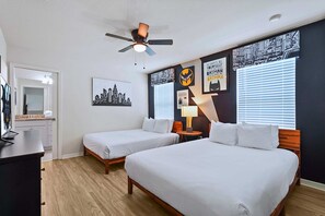 Ein Hotelzimmer mit zwei Betten, einem Deckenventilator, einem Stadtbild, einem Batman-Poster und einem Fenster mit Jalousien.