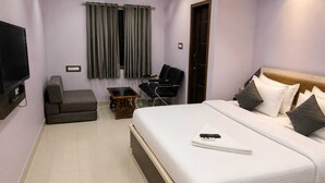 A hotel room with a bed, a TV, a sofa, a chair, and a small table. - Hotel Smile Inn-Next Railway Station (Bhubaneshwar)