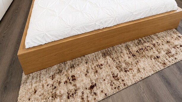 Ein Schlafzimmer mit einem hölzernen Bett, weißer Bettwäsche, einem Teppich, einem Nachttisch mit einer Pflanze und einem an der Wand hängenden abstrakten Gemälde.