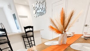 Ein Esstisch ist gedeckt mit orangefarbenen Platzsets, weißen Tellern mit orangefarbenen Rändern und passenden Tassen.