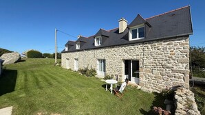 A stone house with a sloped roof, a small lawn, and a white table with chairs outside.