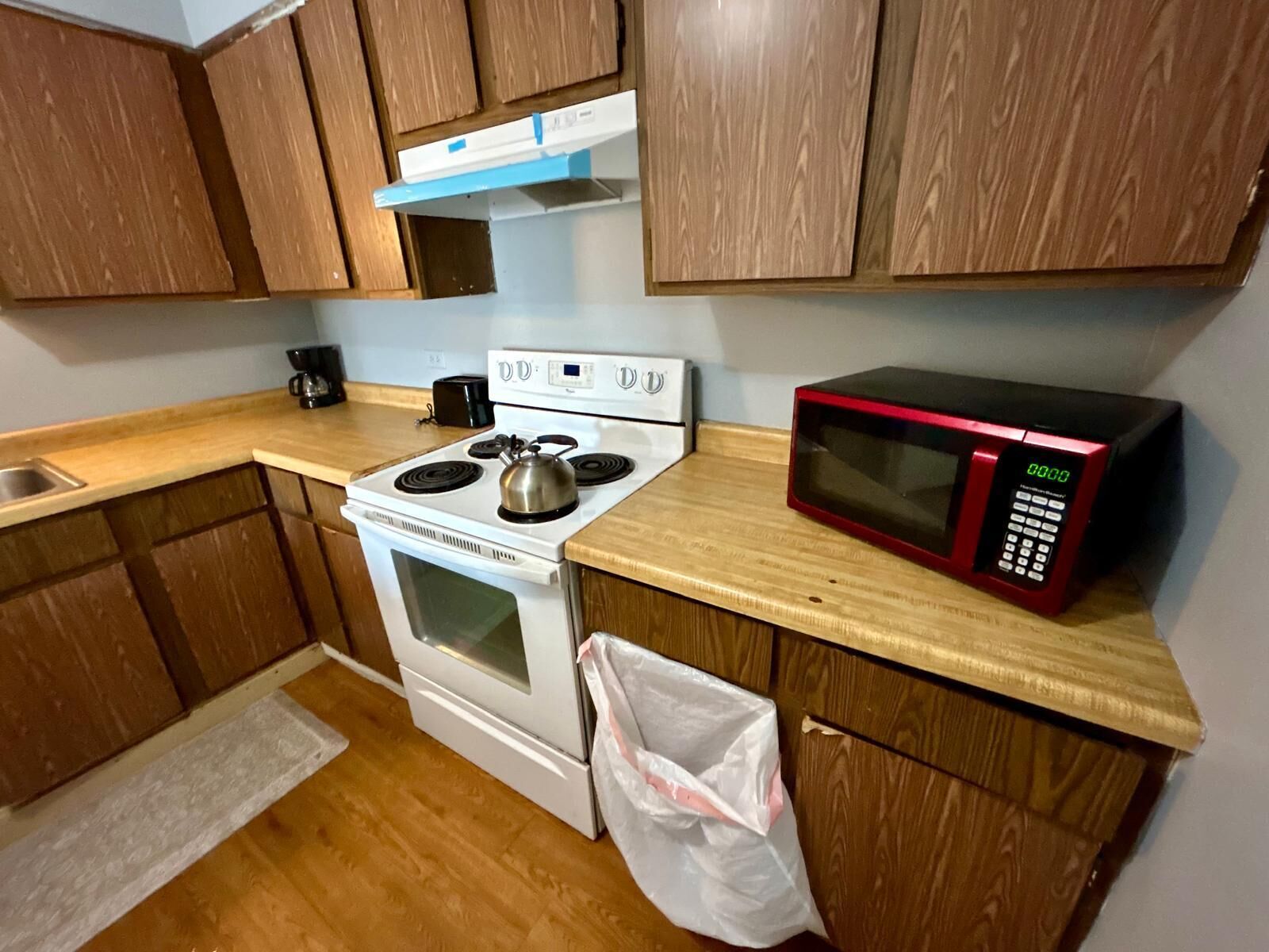 Une cuisine avec des meubles de rangement en bois, une cuisinière blanche, un four à micro-ondes et une machine à café.