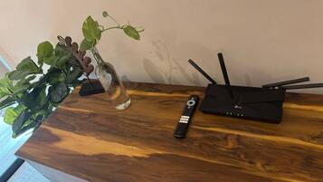 Un tavolo in legno con un vaso di vetro contenente una pianta, un telecomando e un router nero.