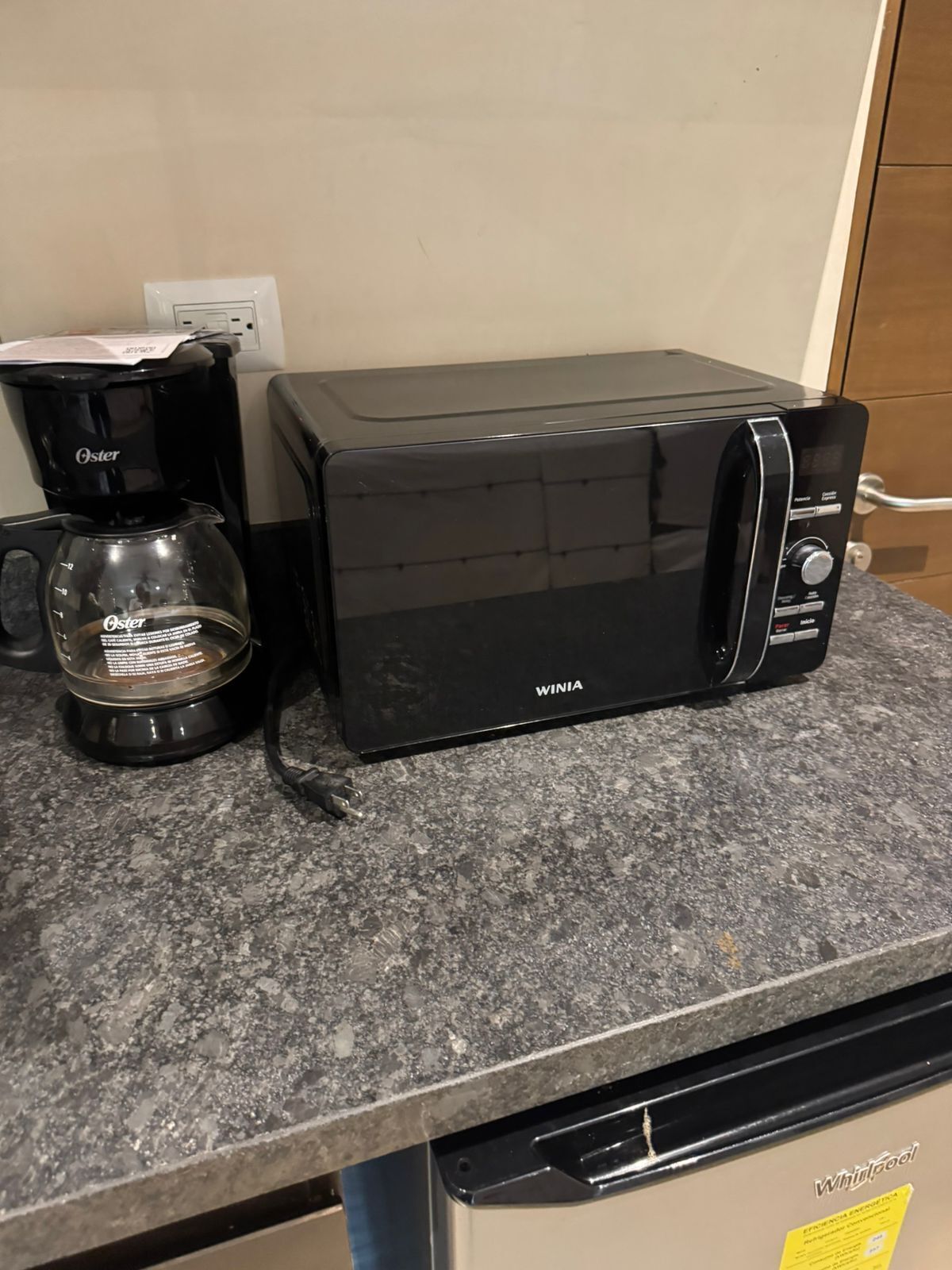 Una cafetera Oster negra y un microondas Winia negros sobre una encimera de granito.