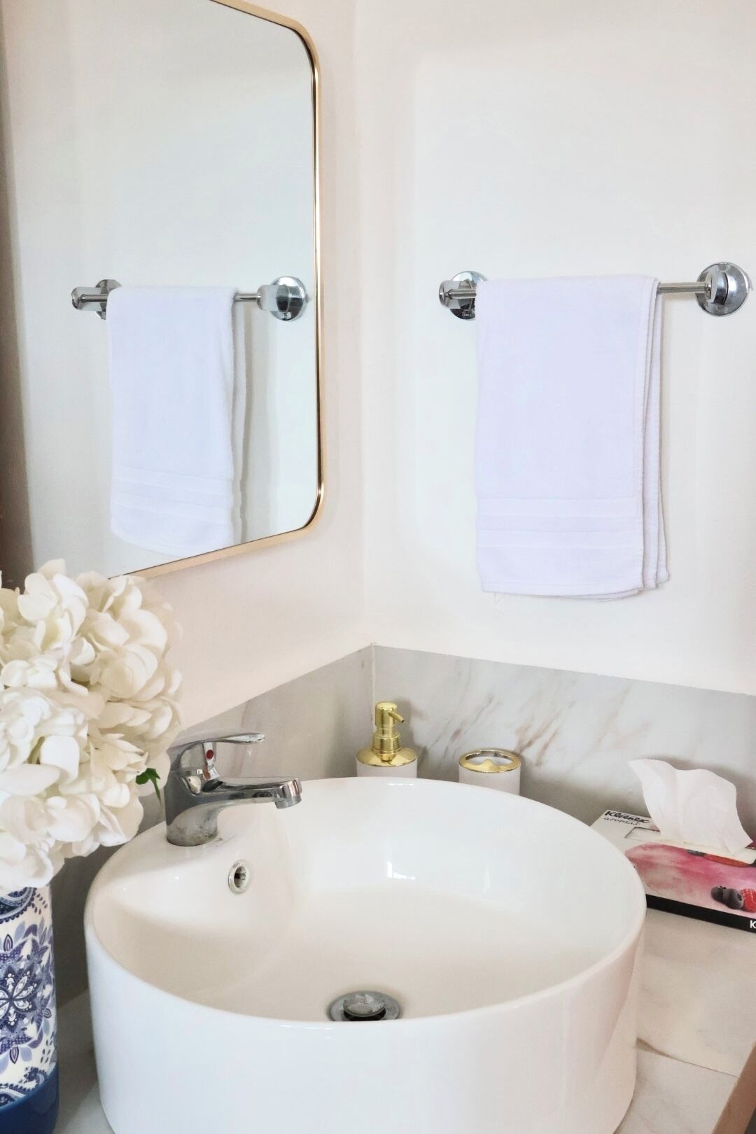 A bathroom with a large white sink, a gold faucet, a mirror with a gold frame, and two white towels hanging on towel bars.