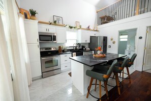 A modern kitchen with white cabinets, stainless steel appliances, a marble countertop island with bar stools, and a wooden staircase. - Boho Luxury Retreat near Winter Garden & Disney - Game Room & Statement Kitchen (Ocoee)